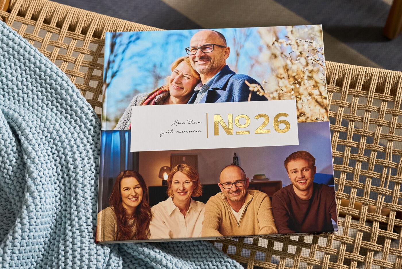 CEWE FOTOBUCH „N°26“ mit Fotos eines Paares und einer Familie von vier Personen auf einem geflochtenen Stuhl mit blauer Decke.